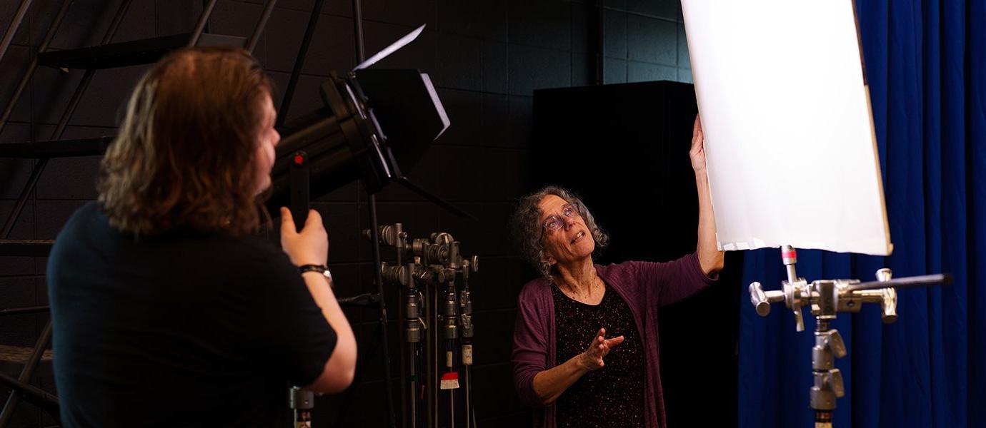 a person talking in front of a person adjusting a light